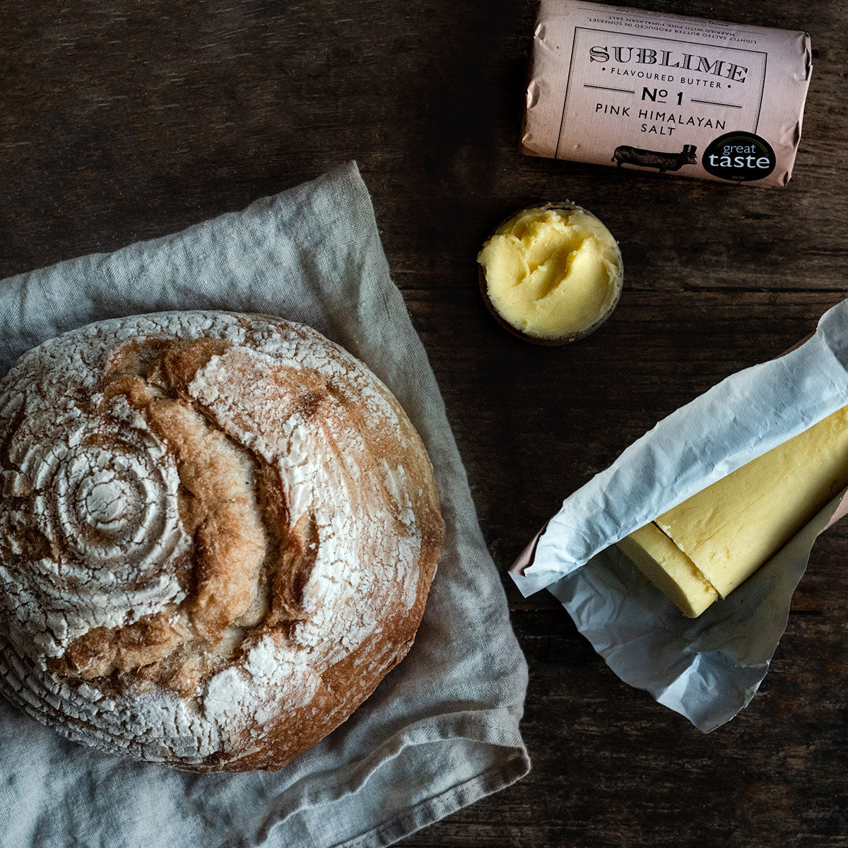 Crusty sourdough bread on a wooden surface, accompanied by Sublime Pink Himalayan Salt butter